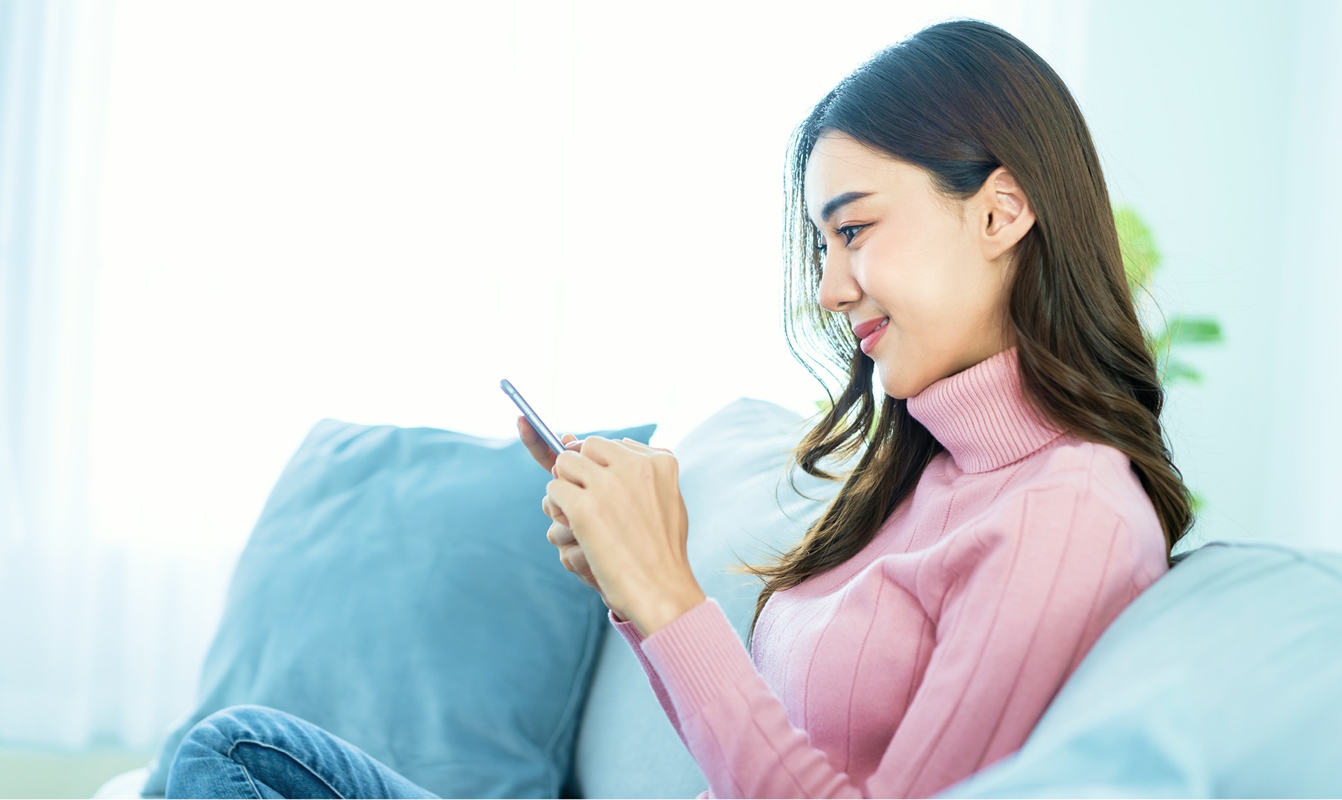 ソファでスマートフォンを見ながら、微笑む女性